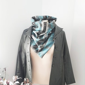 May include: A black leather jacket with a button-up front is displayed on a mannequin. A turquoise, gray, and black patterned scarf is draped around the mannequin's neck. The scarf has a triangular shape.