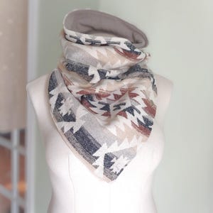 May include: A beige and brown patterned neck warmer with a grey fleece lining. The neck warmer is made of a soft, comfortable fabric and is perfect for keeping warm in the winter.