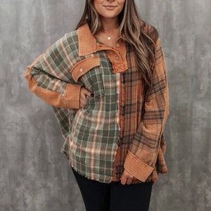May include: A long-sleeved plaid shirt with a patchwork design in shades of green, brown, and orange. The shirt has a collared neckline and a button closure.