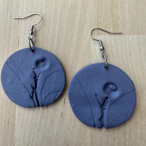 May include: A pair of dark blue round earrings with a floral design. The earrings are made of polymer clay and have silver hooks.