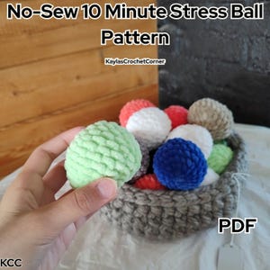 May include: A hand holds a light green, textured stress ball next to a basket filled with various colored stress balls. The basket contains red, white, blue, and green balls. Text on the image reads "No-Sew 10 Minute Stress Ball Pattern" and "PDF".