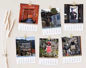 May include: A wall calendar featuring six individual rectangular pages for January through June 2027, each held by a gold binder clip. The pages display photographs of Japanese cultural sites, including torii gates, shrines, and traditional figures.