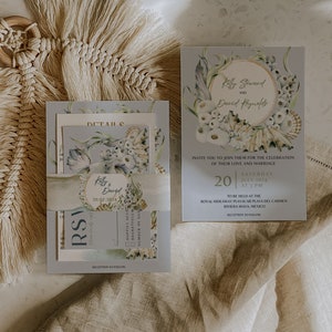 Peut inclure: Une suite d'invitations de mariage avec un motif floral bleu et blanc. L'invitation présente une illustration aquarelle de coquillages et de fleurs. Le texte sur l'invitation indique "Kelly Steward et David Reynolds" et "20 juillet 2024 à 15h00".