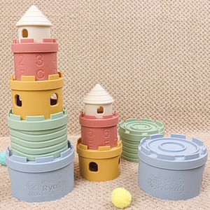 以下が含まれることがあります： パステルカラーの積み重ねタワーおもちゃセット。セットには、城のような構造を形成するために積み重ねることができる複数のピースが含まれています。タワーはピンク、黄色、緑、青の色合いで、白い上部が付いています。一部のピースには数字と名前が記載されています。