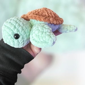 May include: A crocheted turtle toy with a light green body and brown shell. The turtle has black eyes and a soft, fuzzy texture.