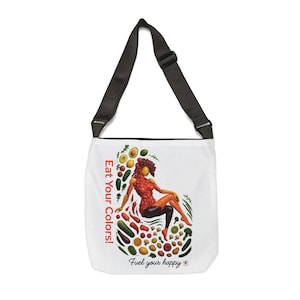 Puede incluir: Bolso tote blanco con una correa negra ajustable. El bolso presenta una colorida ilustración de una persona hecha de verduras y frutas, con el texto "Eat Your Colors!" y "Fuel your happy".