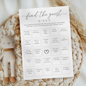 以下が含まれることがあります： 「find the guest」と書かれた黒い文字の白いビンゴゲームカード。カードには、さまざまなプロンプトを含むボックスのグリッドがあります。茶色のスカーフが付いたぬいぐるみウサギのおもちゃが、織られた表面のカードの隣にあります。