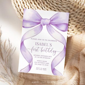 May include: A white invitation card with a large, watercolor-style lavender bow. The text reads "PLEASE JOIN US TO CELEBRATE ISABEL'S first birthday" with event details. The card is set against a neutral background.