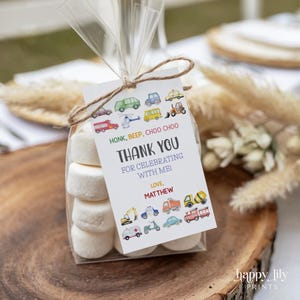 Könnte beinhalten: Ein klarer Zellophanbeutel mit Marshmallows, gebunden mit Bindfaden und einem Anhänger. Der Anhänger lautet: "HONK, BEEP, CHOO CHOO THANK YOU FOR CELEBRATING WITH ME! LOVE, MATTHEW" mit Fahrzeugillustrationen.
