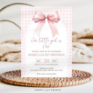 May include: Pink and white gingham patterned invitation with a pink bow. The text reads "Our little girl is One. Please join us to celebrate Isabella's 1st Birthday. Sat 28 Oct from 3 to 5 in the afternoon. Isabella's House 123 Happy Lily Lane, Seattle, WA, 92119. RSVP to Mom 123.456.7890. Happy Lily Prints."