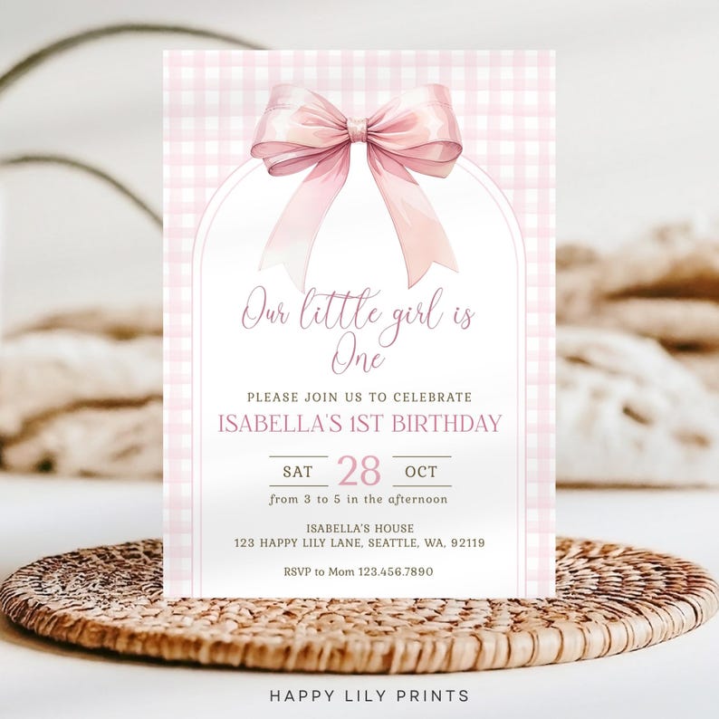 May include: Pink and white gingham patterned invitation with a pink bow. The text reads "Our little girl is One. Please join us to celebrate Isabella's 1st Birthday. Sat 28 Oct from 3 to 5 in the afternoon. Isabella's House 123 Happy Lily Lane, Seattle, WA, 92119. RSVP to Mom 123.456.7890. Happy Lily Prints."