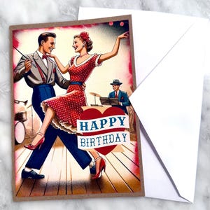 May include: A vintage-style birthday card featuring a couple dancing, with a band in the background. The woman wears a red polka-dot dress, and the man is in a suit. The card has a heart with the words "Happy Birthday" and comes with a white envelope.