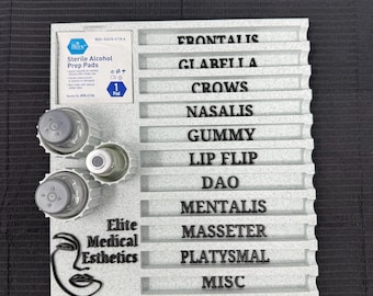 May include: A light gray esthetics tray with the text "Elite Medical Esthetics" and a stylized face logo. The tray has labeled slots for procedures like "Frontalis" and "Gummy", and includes alcohol prep pads and small bottles.