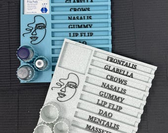 May include: Two trays, one light blue and one gray, with labeled sections for cosmetic procedures. The trays feature a line art face design and hold small containers. The light blue tray has the text "FRONTALIS, CLABELLA, CROWS, NASALIS, GUMMY, LIP FLIP".