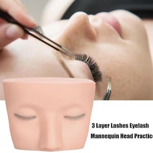Può includere: Una testa di manichino con ciglia applicate su un occhio. La testa è realizzata in silicone rosa chiaro e ha un aspetto realistico. La testa viene utilizzata per esercitarsi nell'applicazione delle ciglia. Il testo "3 Layer Lashes Eyelash Mannequin Head Practice" è visibile nell'immagine.