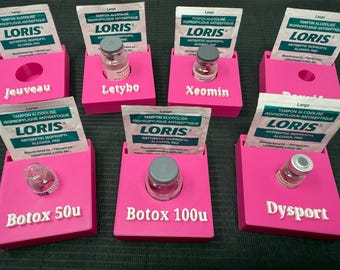 Puede incluir: Una exhibición de contenedores rosas, cada uno con un vial y una almohadilla de alcohol antiséptico. Los contenedores están etiquetados con nombres como "Jeuveau", "Letybo", "Xeomin", "Botox 50u", "Botox 100u" y "Dysport".