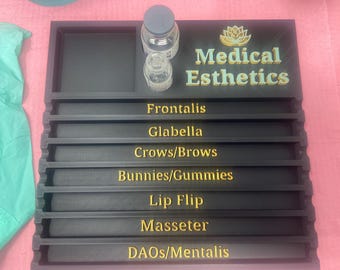 May include: Black tray with gold lettering for medical esthetics. The tray has seven compartments labeled: Frontalis, Glabella, Crows/Brows, Bunnies/Gummies, Lip Flip, Masseter, DAOs/Mentalis.