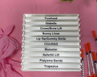 May include: A white plastic tray with 10 slots labeled with different areas of the face for cosmetic injections. The labels include Forehead, Glabella, Crows/Brow Lift, Bunny Lines, Lip flip/Gummy Smile, Chin/DAO, Masseter, Nefertiti Lift, Platysma Bands, and Trapezius.