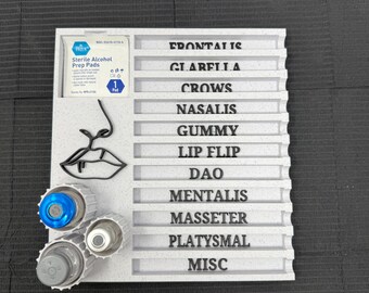 May include: A gray plastic organizer with labeled sections for facial muscles, including "FRONTALIS" and "MASSETER." It features a drawing of a nose and lips, along with three contact lens cases and a sterile alcohol prep pad.