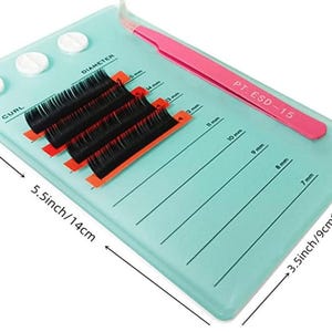 Op de afbeelding: Een turquoise blauwe wimpertray met een roze pincet en een set zwarte wimperextensions. De tray heeft een liniaal met maatverdelingen in millimeters en een label met de tekst "PT. ESD-15".