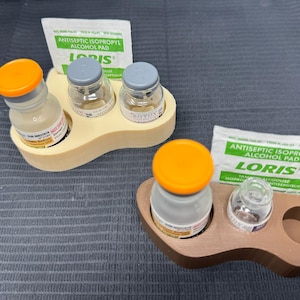 May include: Two trays, one beige and one brown, each holding vials and a small packet. The beige tray has three vials, two with grey caps and one with an orange cap. The brown tray has one vial with an orange cap and one clear vial.