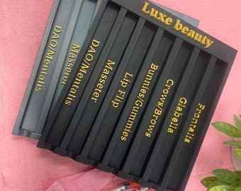 May include: Black plastic tray with gold lettering labeled "Luxe beauty" and the names of different facial injection areas, including Frontalis, Glabella, Crows/Brows, Bunnies/Gummies, Lip Flip, Masseter, and DAO/Mentalis.