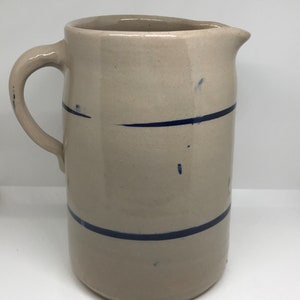 Puede incluir: Una jarra de cer&aacute;mica vintage de color crema con un dise&ntilde;o de rayas azules. La jarra tiene una boca ancha y un asa.