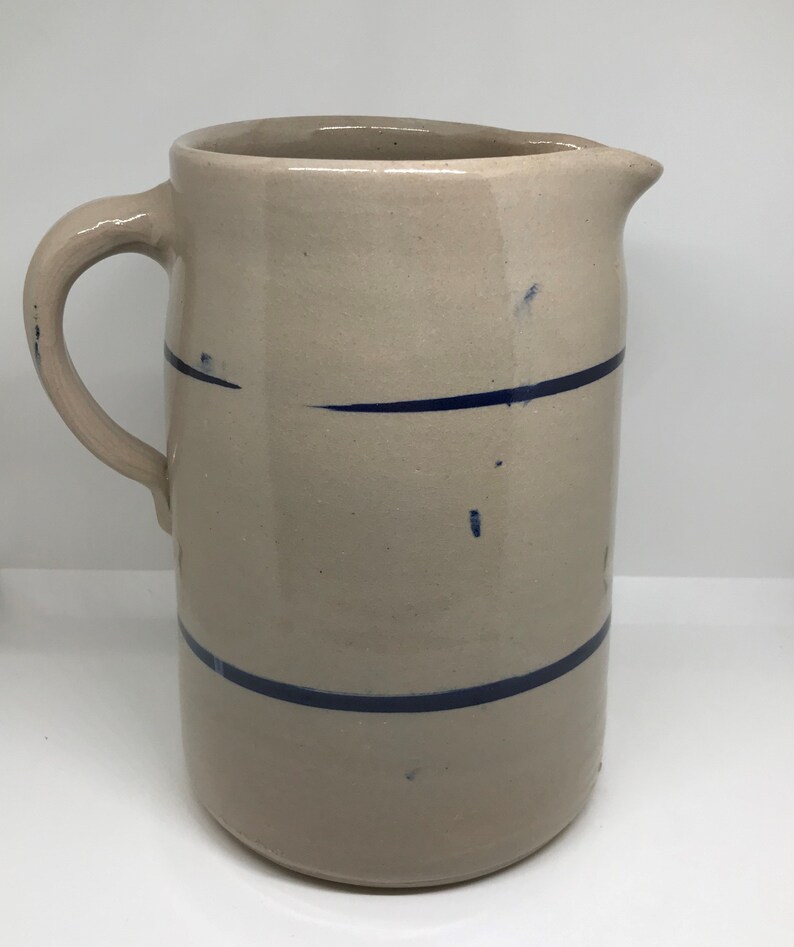 Puede incluir: Una jarra de cer&aacute;mica vintage de color crema con un dise&ntilde;o de rayas azules. La jarra tiene una boca ancha y un asa.