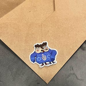 May include: Two cartoon characters wearing a blue sweater with a Star of David and a dreidel design. The characters are smiling and have a festive look.