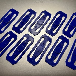 Peut inclure: Huit boucles en plastique bleu avec un centre arrondi de forme ovale. Les boucles sont disposées en deux rangées de quatre.