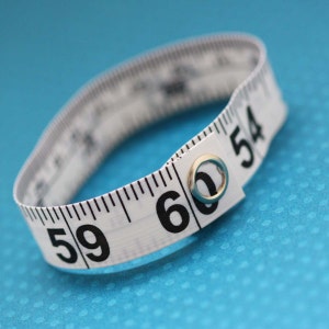 May include: A white measuring tape with black markings, curled into a circle. The numbers 59, 60, and 54 are visible on the tape.