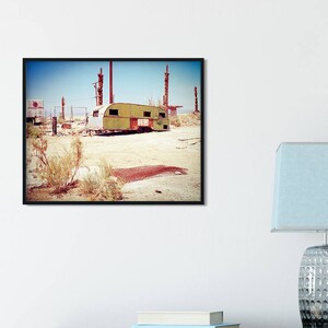 Può includere: Un camper vintage verde e giallo si trova in un paesaggio desertico con pali di metallo arrugginiti sullo sfondo.