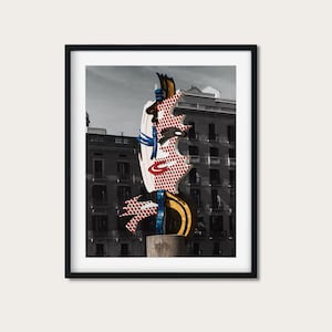 Könnte beinhalten: Eine große, farbenfrohe, abstrakte Skulptur eines Gesichts mit roter, weißer, blauer und gelber Farbe. Die Skulptur steht vor einem Gebäude mit Fenstern.