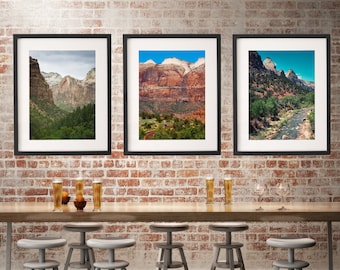 May include: Three framed landscape photographs of a mountainous region with a river running through it. The photos are hanging on a brick wall above a wooden table with six bar stools.