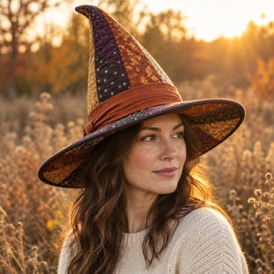 Può includere: Un cappello alto e a punta caratterizzato da un design patchwork trapuntato nei toni del viola scuro, arancione bruciato e oro con piccoli motivi a stella. Il cappello presenta una tesa larga e strutturata e una fascia in tessuto arancione.