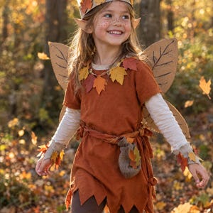 May include: A costume featuring a rust-colored tunic with a jagged hem, a leaf-adorned crown, and matching wrist cuffs. The outfit includes a small pouch tied at the waist, a collar of autumn-colored leaves, and large, tan, leaf-shaped wings.