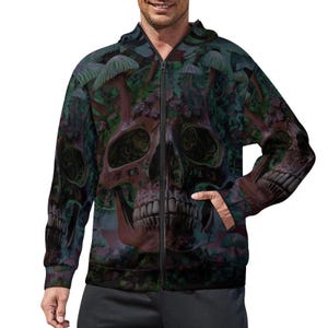 Puede incluir: Una sudadera con capucha y cremallera de manga larga con un estampado integral de un gran cráneo humano centrado en la parte delantera, rodeado de follaje forestal verde oscuro y morado e ilustraciones de setas, con una cremallera frontal negra.