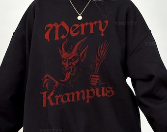 May include: Black sweatshirt with the words "Merry Krampus" in red gothic lettering. A red Krampus illustration is centered below the text, holding a bundle of birch branches. The sweatshirt has long sleeves and a crew neck.