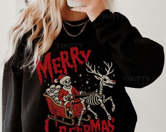 May include: Black sweatshirt with a red graphic that says "MERRY CREEPMAS". The graphic features a skeleton Santa Claus in a sleigh pulled by a skeleton reindeer. The sweatshirt is paired with black and white checkered pants.