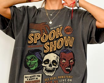 May include: Dark gray t-shirt with a vintage-style "Spook Show" graphic. The design features a witch, skull, and vampire, with text reading "Get Ready for a Night of Horrors!" and "See Real Monsters! Live on Oct 31 Stage."