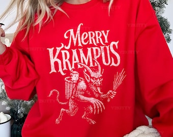 May include: A red sweatshirt with the words "Merry Krampus" in a vintage font. The graphic depicts Krampus carrying a child in a basket. The design is in white. A festive holiday-themed apparel item.