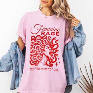 May include: Pink t-shirt with a red graphic of a woman with snakes for hair. The text "Feminine Rage" is above the graphic and "Girls will be girls. Stone cold since 700 BC" is below the graphic.