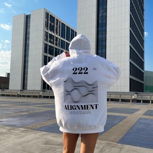 May include: White hoodie with a black and white graphic print on the back. The graphic features a wavy design with the text "222" and "ALIGNMENT" below it.