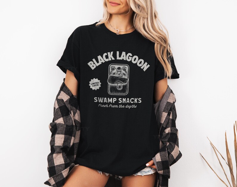 May include: Black t-shirt with the text "Black Lagoon" above a graphic of a creature in a lunchbox, with the words "Swamp Snacks" and "Fresh from the depths" below. The shirt also has a "Limited Catch" graphic.