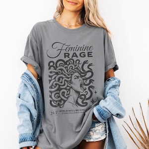 May include: A gray t-shirt with a graphic of a woman with snakes for hair. The text "Feminine Rage" is above the graphic and the text "24/7 Girls will be girls, stone cold since forever" is below the graphic.