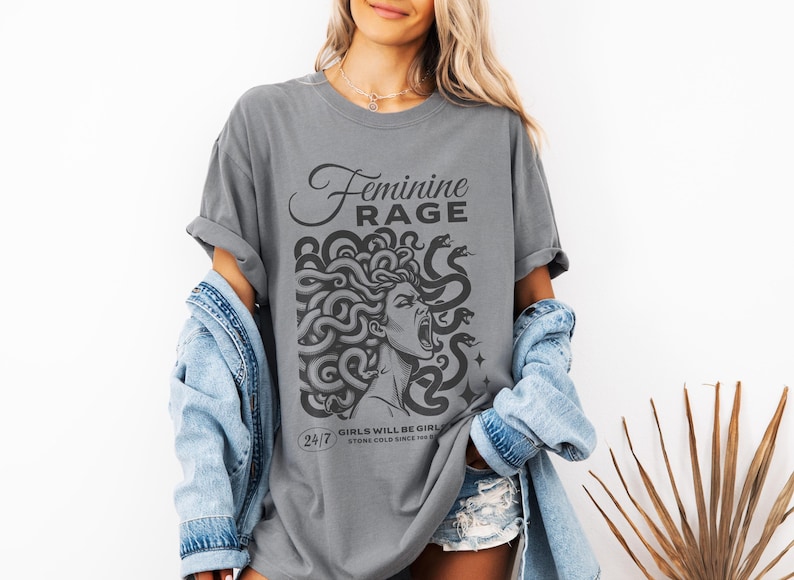 May include: A gray t-shirt with a graphic of a woman with snakes for hair. The text "Feminine Rage" is above the graphic and the text "24/7 Girls will be girls, stone cold since forever" is below the graphic.
