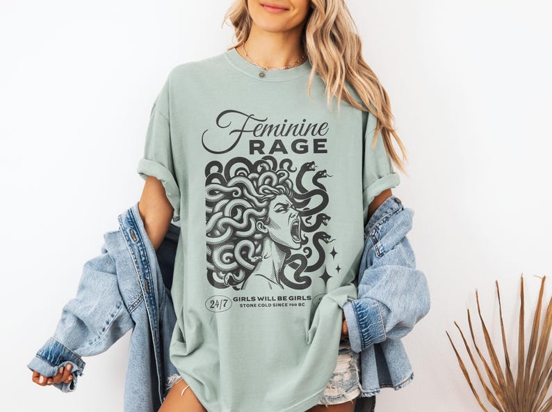 May include: A light green t-shirt with a graphic print of a woman with snakes for hair. The text "Feminine Rage" is printed above the graphic. The text "Girls will be girls. Stone cold since 70 BC" is printed below the graphic.
