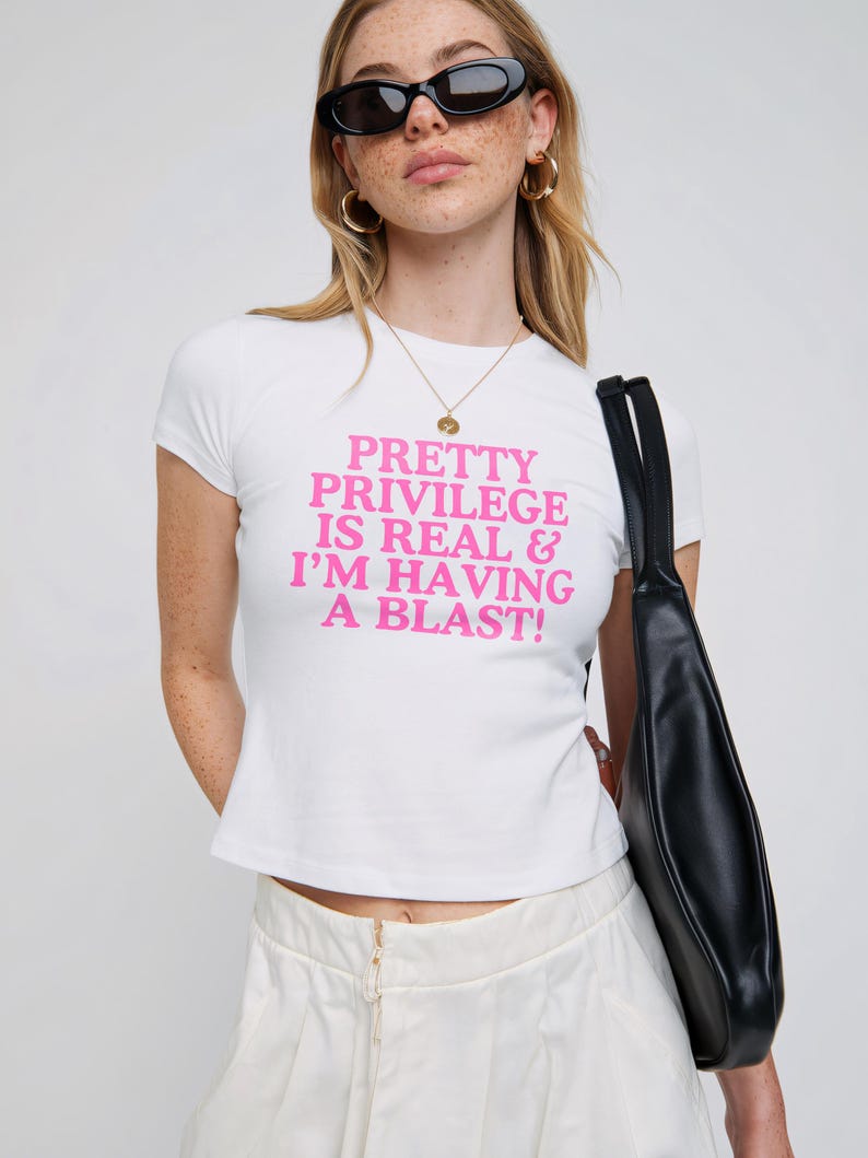 May include: White cropped t-shirt with pink text that reads "PRETTY PRIVILEGE IS REAL & I'M HAVING A BLAST!"