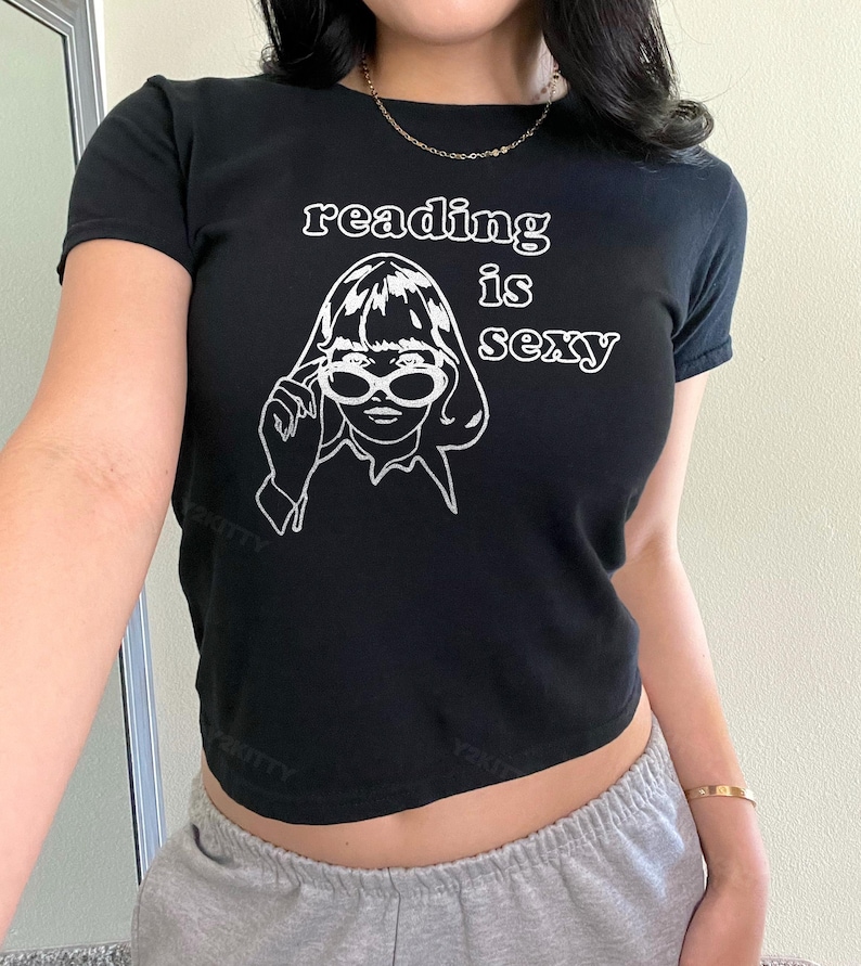 May include: Black crop top with the text "reading is sexy" and a white graphic of a woman wearing sunglasses. The shirt has short sleeves and a round neckline. The overall style is casual and trendy.
