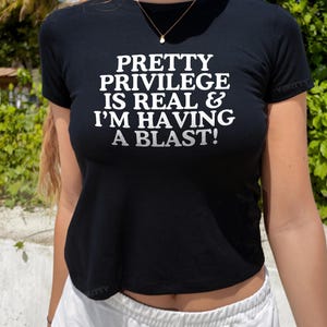 May include: A black cropped t-shirt with the text "PRETTY PRIVILEGE IS REAL & I'M HAVING A BLAST!" printed in white.